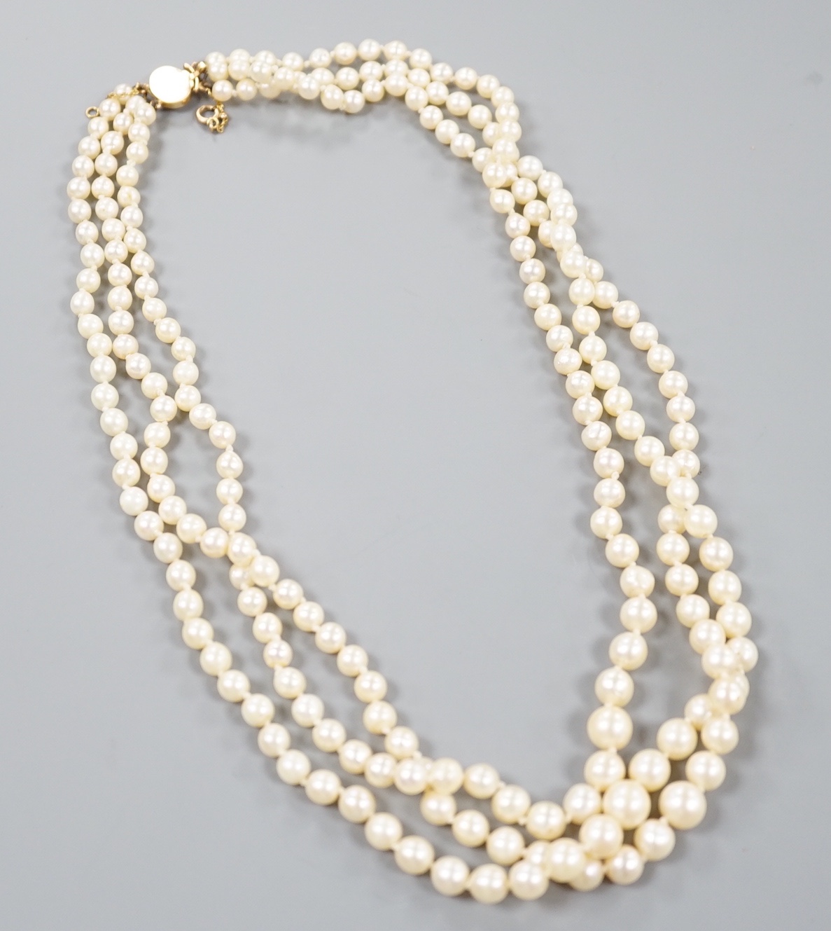 A triple strand graduated cultured pearl necklace, with yellow metal clasp, 50cm.